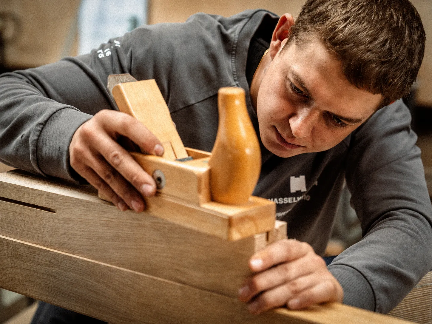 Schreiner bearbeitet ein Holzbauteil sorgfältig mit einem Handhobel