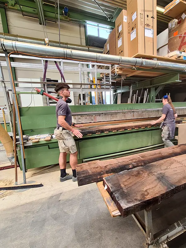 Mitarbeiter bearbeiten das Holz für den Esstisch an einer Maschine.