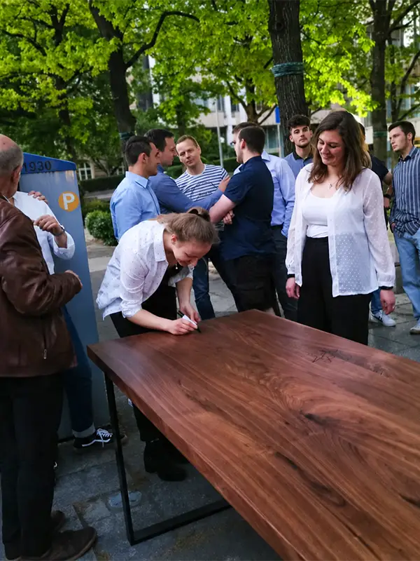 Das Team signiert den selbst gefertigten Esstisch als persönliches Geschenk.