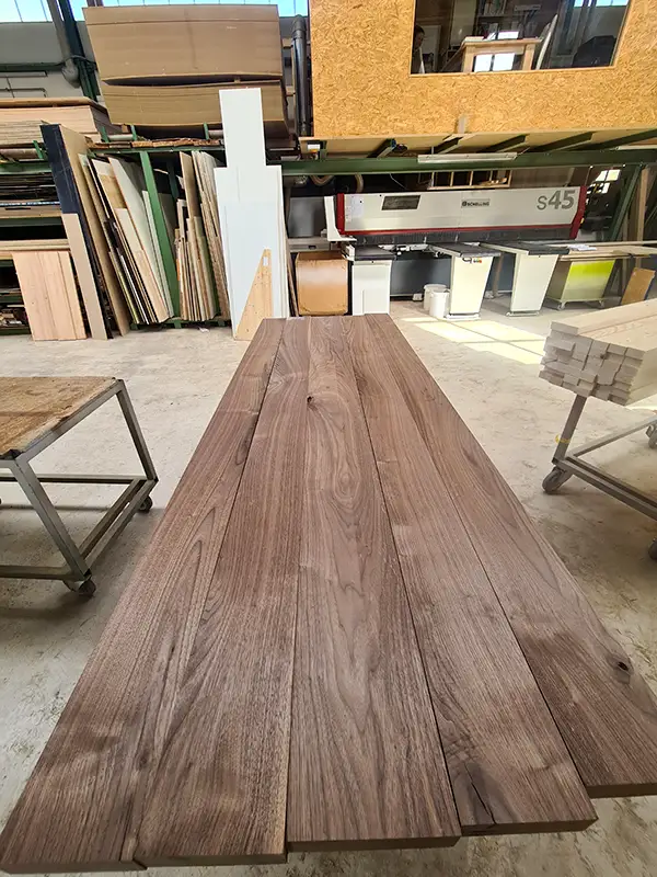 Zugeschnittene Holzbretter für den Esstisch liegen in der Werkstatt bereit.